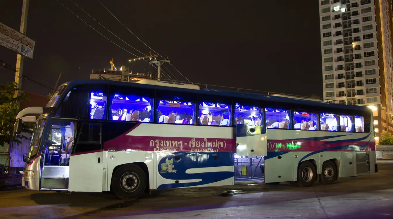 Side view of a long-distance passenger bus in Thailand with an open luggage compartment beneath the seating area.