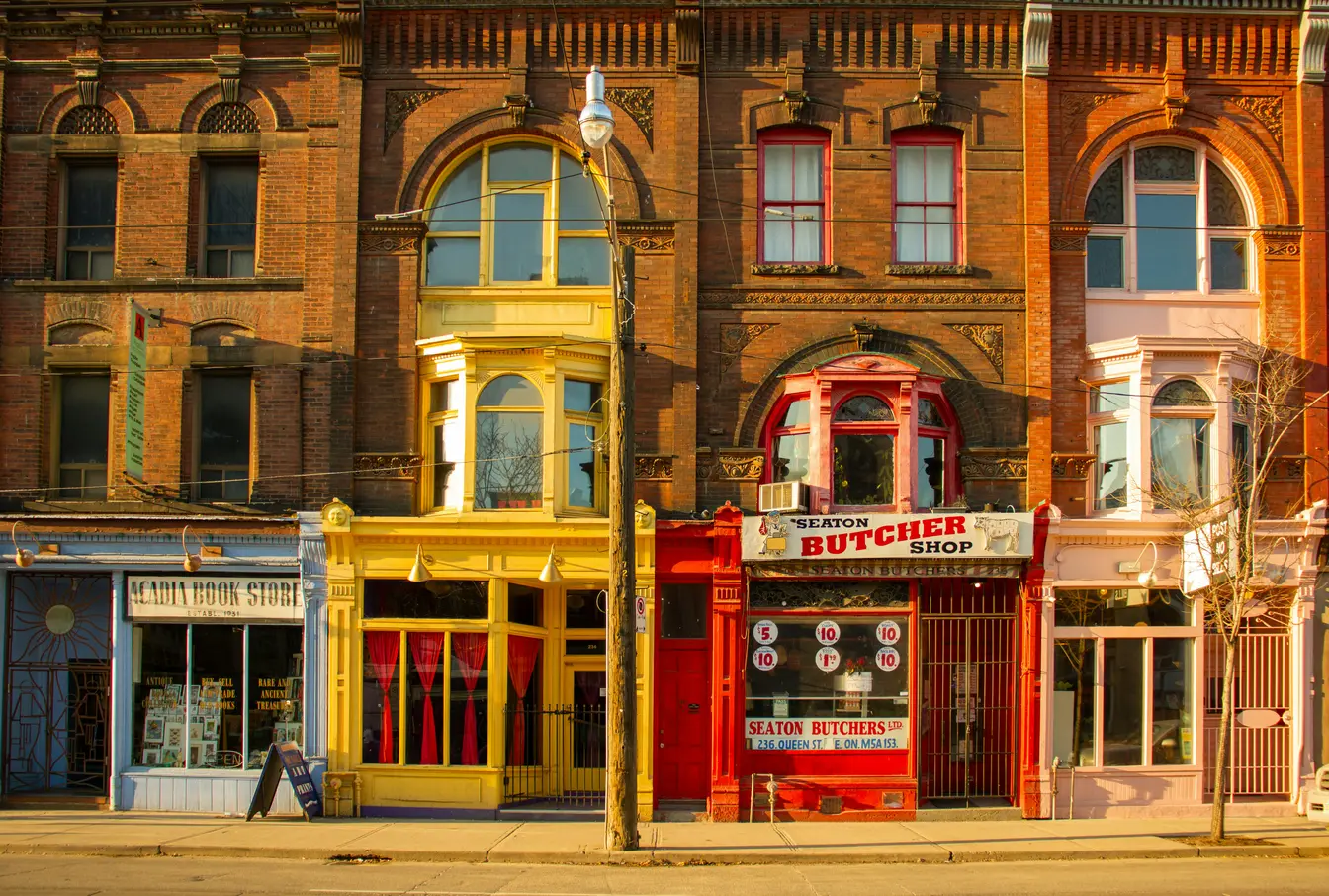  Imagen que muestra una fila de edificios comerciales y residenciales históricos de estilo victoriano situados en la calle Queen Street East, en Toronto.