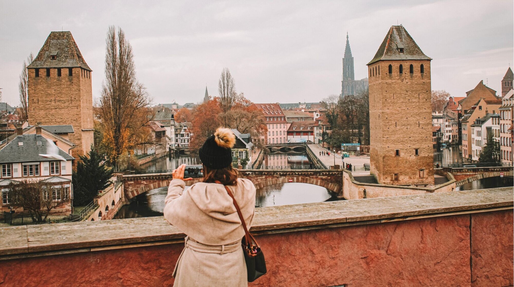 Imagem de uma mulher tirando uma foto das famosas Ponts Couverts em Estrasburgo.