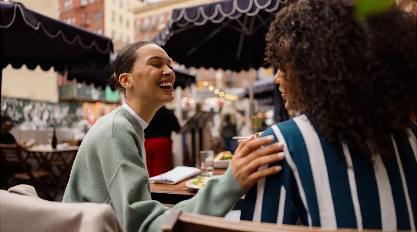 Amigas rindo aproveitando o brunch em restaurante ao ar livre em Nova York.