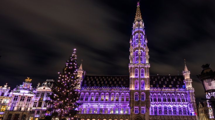 A colour image showing the buildings of the Grand Place in Brussels by night, lit up with purple lights. To illustrate a blog post entitled 'Extreme Day Trips: Eurostar Christmas Markets Edition'.