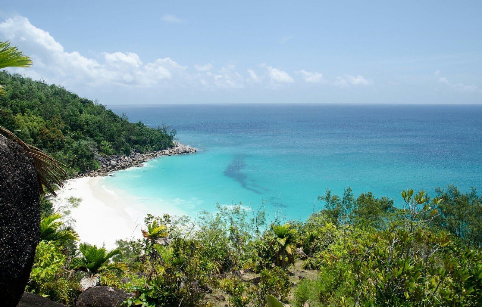 Ein weißer Strand mit blauem Wasser auf der Insel Praslin an einem sonnigen Tag zur Regenzeit auf den Seychellen.
