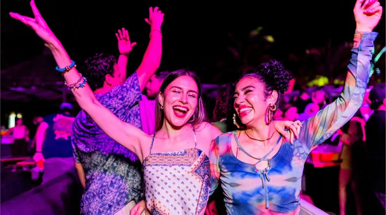 Dos mujeres bailando y celebrando en una fiesta de spring break en México con luces de colores.