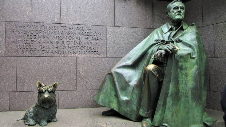 A photograph of a bronze statue of Fala the Scottish Terrier sitting at the feet of President Franklin D. Roosevelt in Washington D.C.’s FDR Memorial. The dog’s head is raised proudly beside his owner’s flowing cloak.