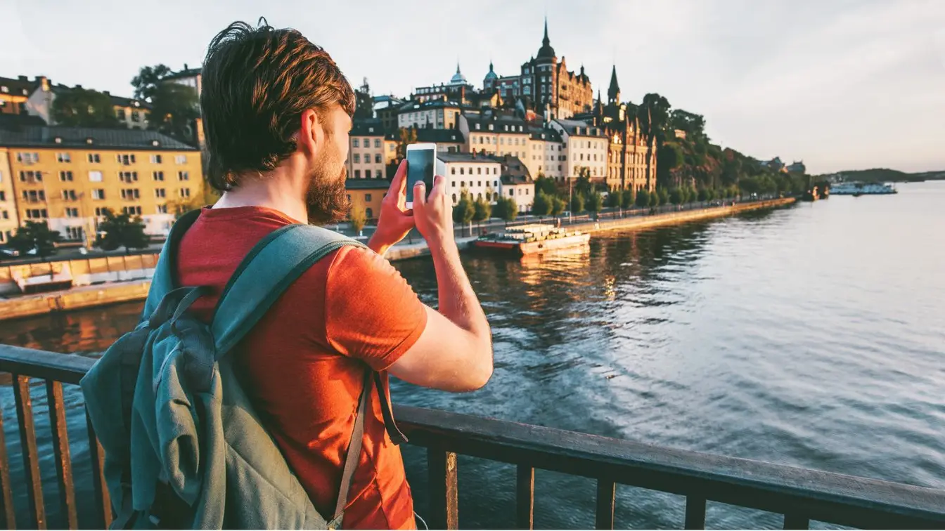 Ein Tourist in Schweden während Midsommar schaut auf sein Handy am Wasser