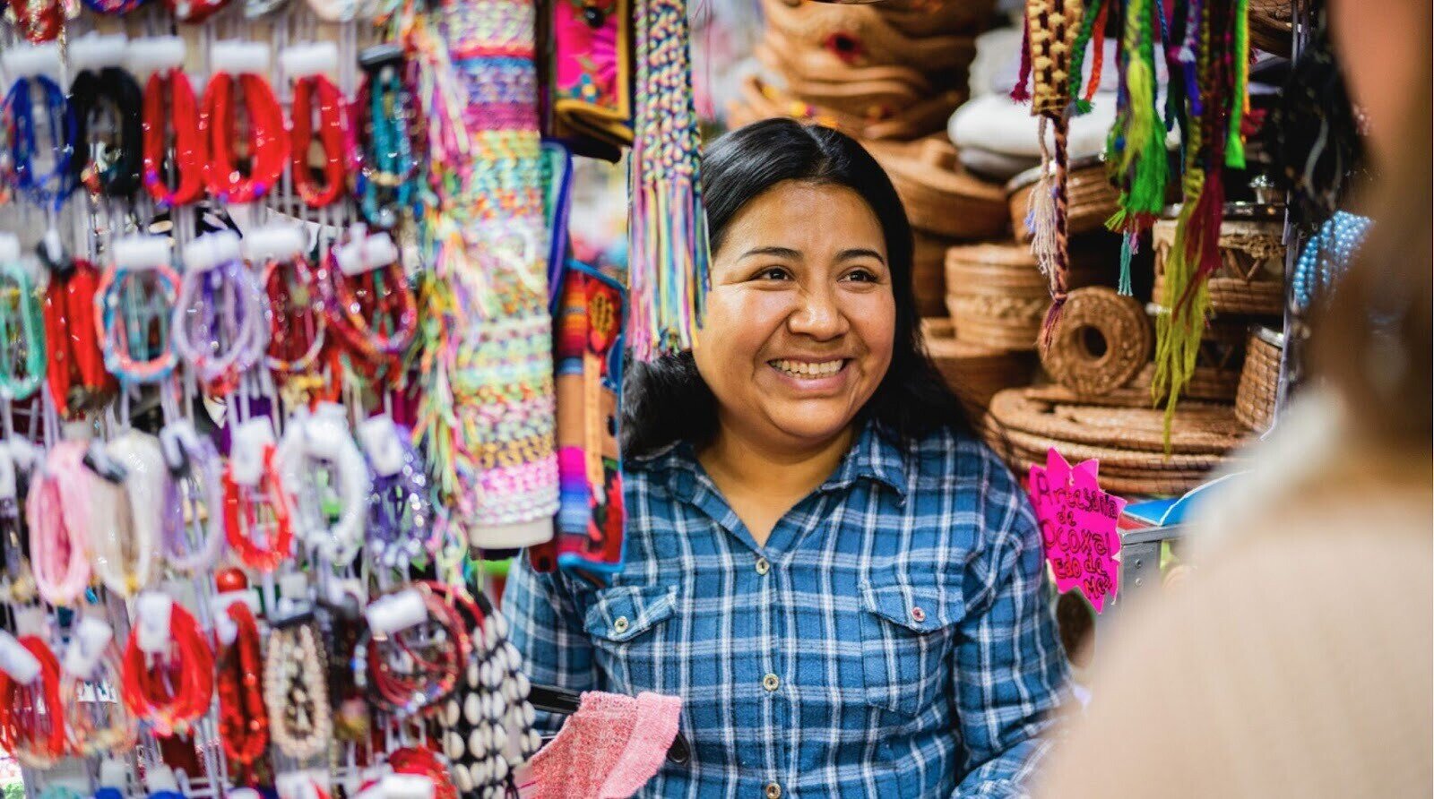 Vendedora mexicana olhando para cliente em sua loja de souvenirs e acessórios locais.