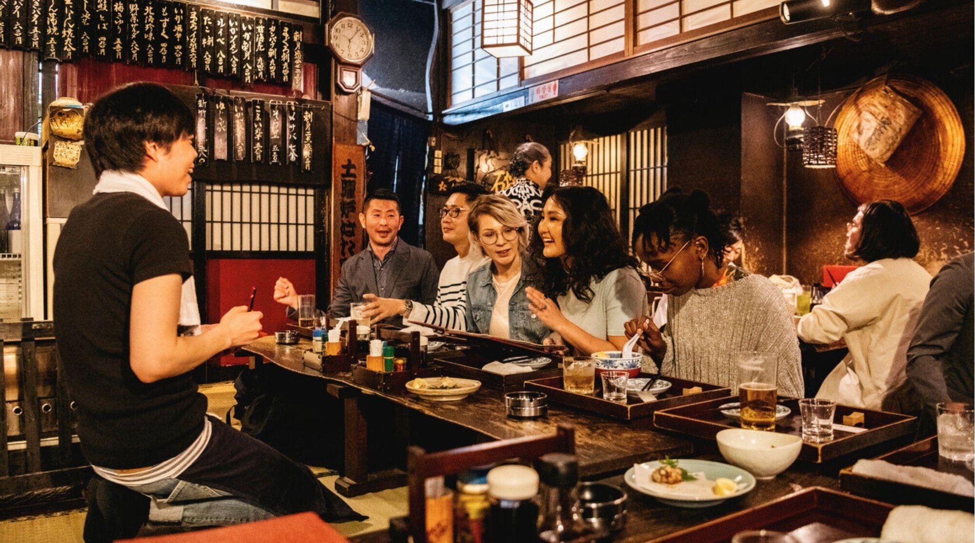 Grupo de amigos latinos pidiendo comida en un izakaya tradicional en Japón.
