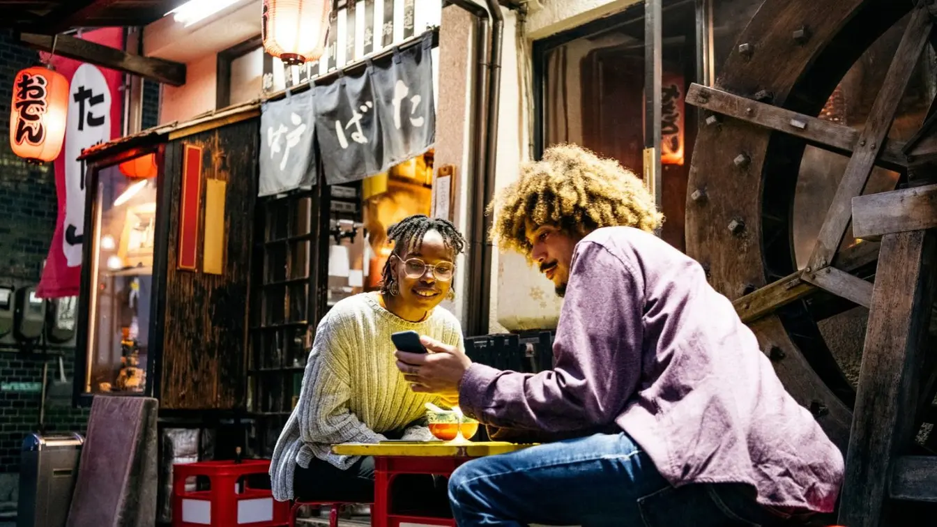 A couple looking at a phone while sitting at a table outside a Japanese izakaya.