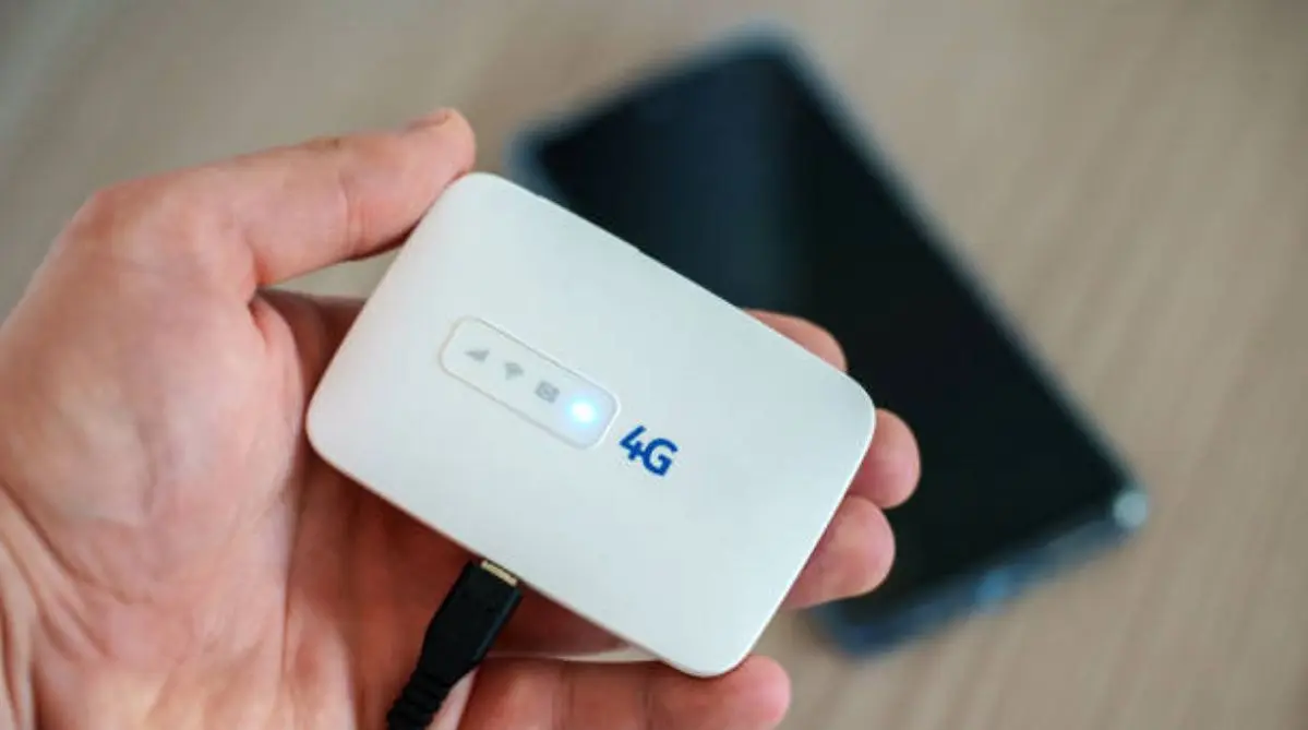 Una persona sostiene un router Wi-Fi portátil 4G junto a su teléfono.