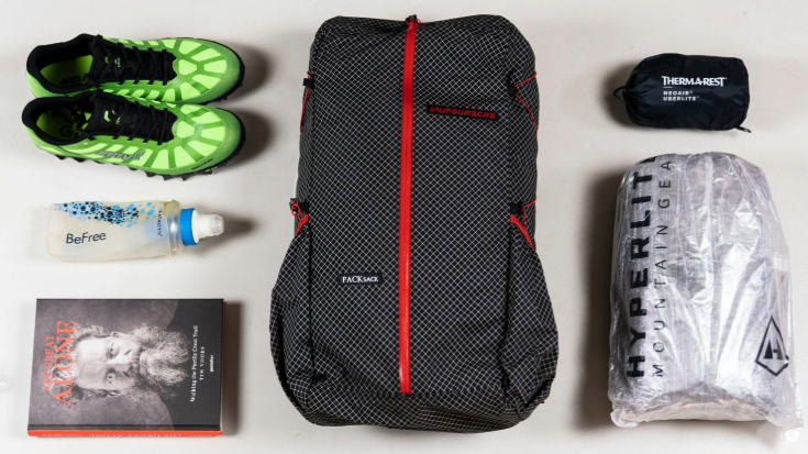 A colour photograph of a plain white floor with someone's holiday packing spread out on it. There are a pair of neon green trainers, an empty water bottle, a backpack and some clothes wrapped tightly in waterproof plastic. There is also a paper book. To illustrate a blog post entitled 'Berlin Half Marathon 2026​: Can You Still Register?'