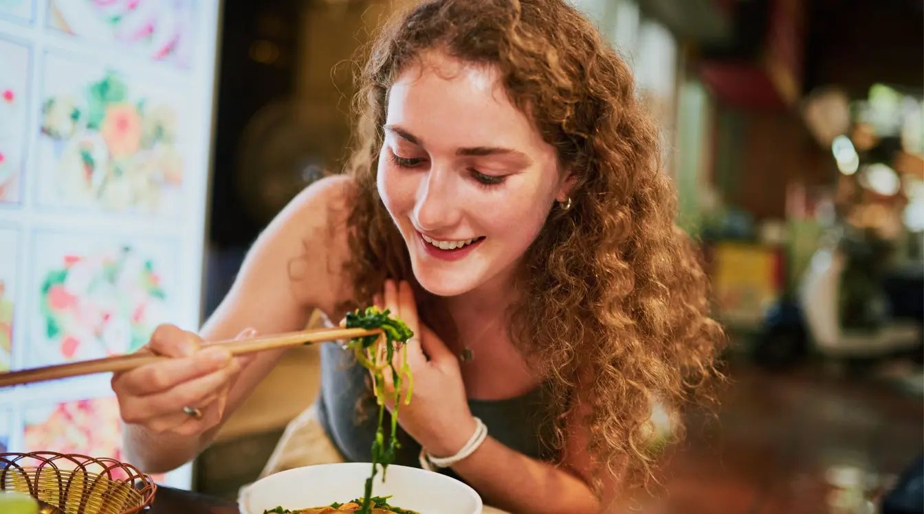 Eine junge Frau genießt lächelnd das Essen auf einem Markt in Vietnam