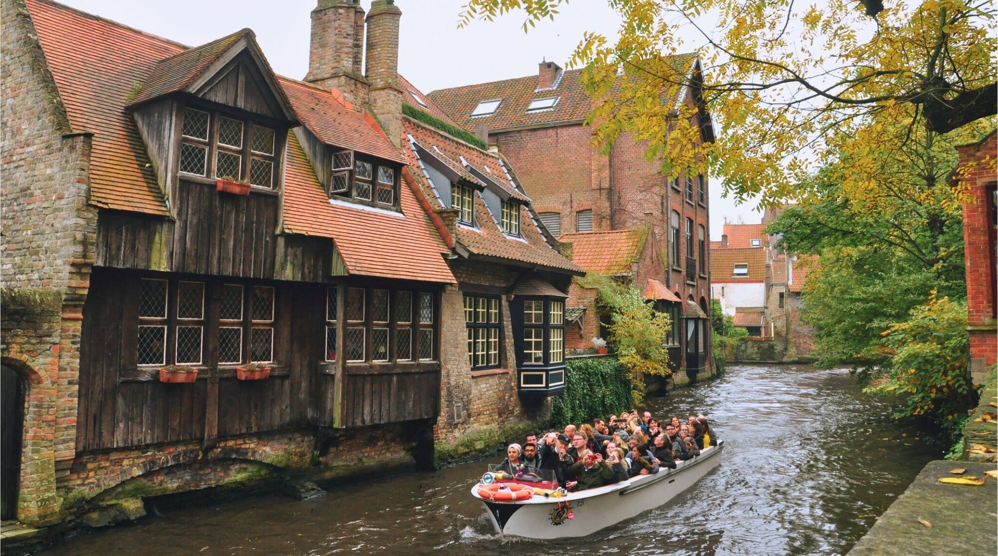 Viajantes em barcas pelos canais de Bruges cercados de prédios de arquitetura medieval.