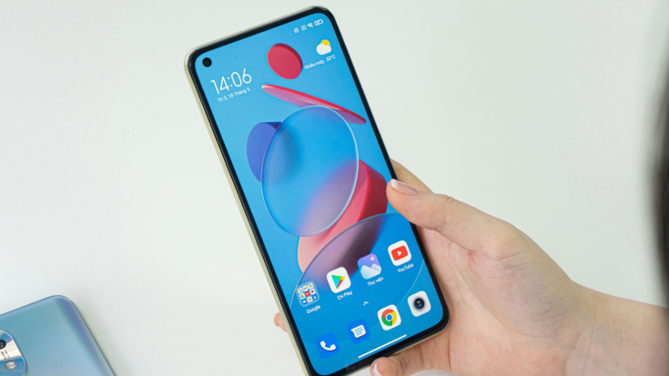 A photograph of a hand holding a Xiaomi Mi 11 Lite 5G mobile telephone. The screen is showing the startup menu, which includes app icons such as Google Play store, YouTube and Image Viewer. To illustrate a blog post entitled 'Are Xiaomi Phones eSIM Compatible in 2025?.' 