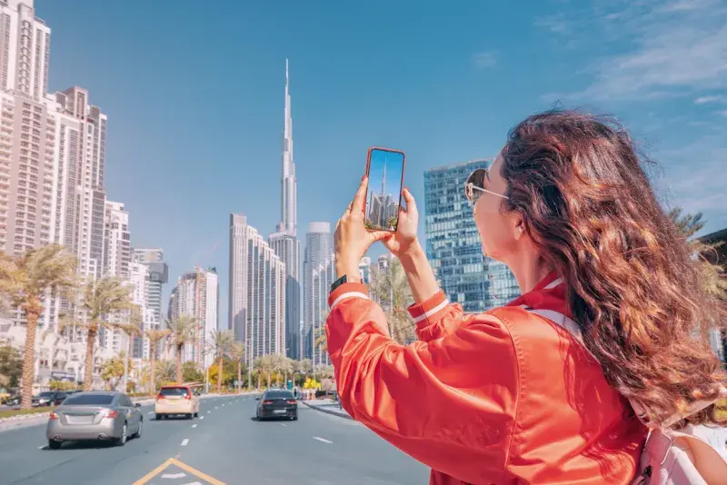 Turista fotografiando el skyline de Dubái con su teléfono mientras viaja con eSIM internacional para varios países.