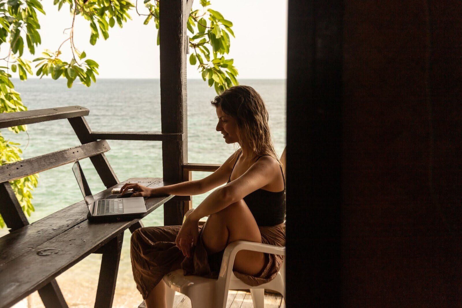 Eine Frau arbeitet mit Laptop am Strand in Thailand