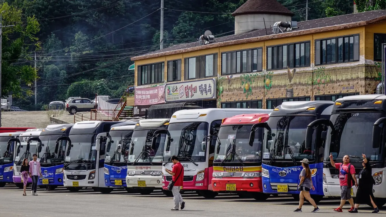 韓国観光地の駐車場に停まる複数の大型観光バスと旅行客