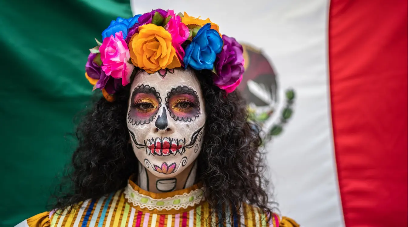 Femme maquillée en Catrina tenant un drapeau mexicain pendant le Día de los Muertos au Mexique.