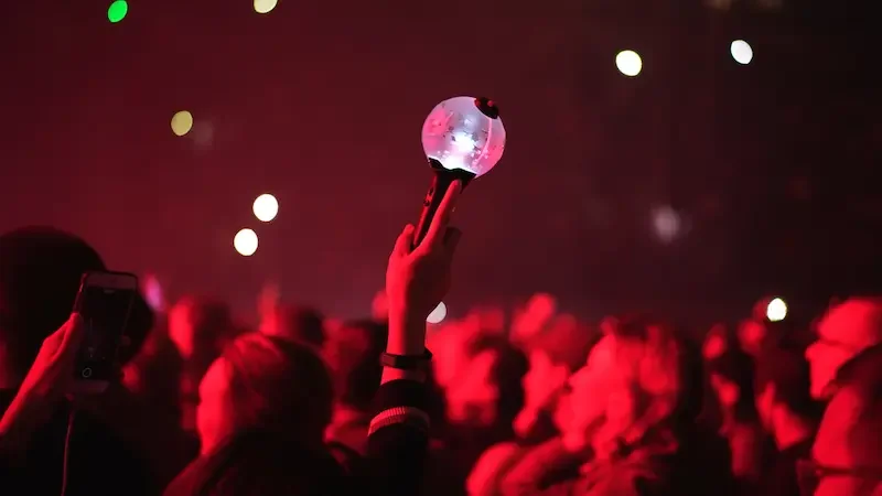 K-POPの韓国ライブ会場で、ペンライト（応援棒）を掲げて盛り上がる観客と赤いステージ照明