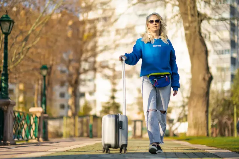 Femme tenant faisant rouler une valise blanche sur des pavés en ville