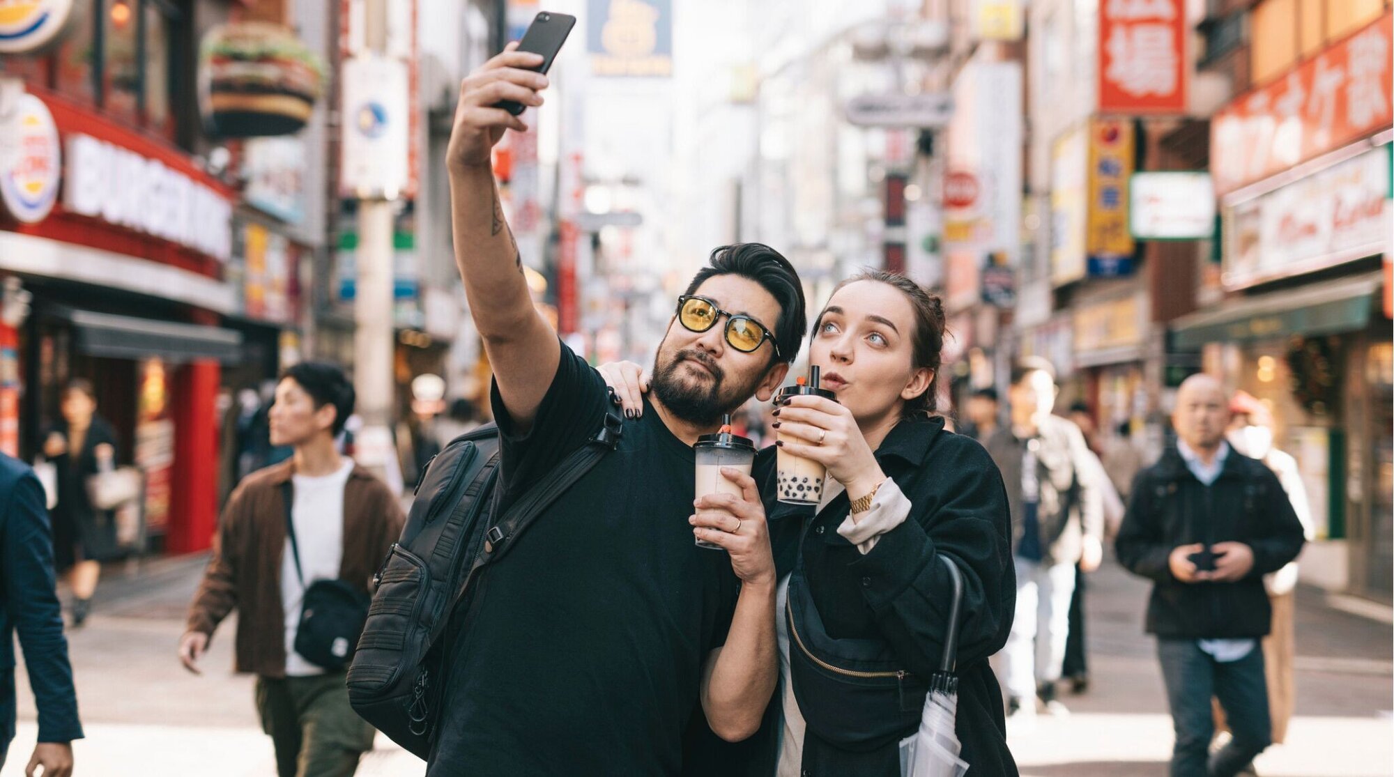 Casal de turistas no Japão tirando selfie com bebidas enquanto aproveitam a viagem conectados ao celular com chip internacional Japão.