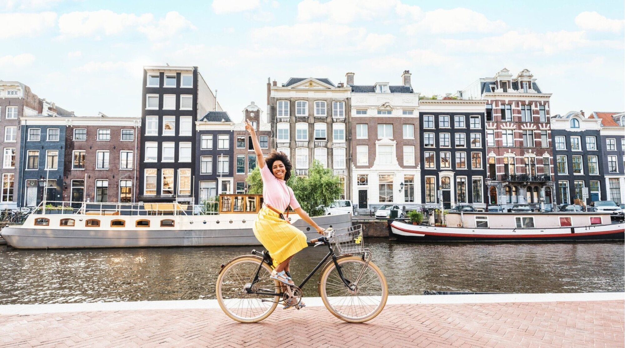Turista feliz visitando Amsterdã, nos Países Baixos, país do espaço schengen. Mulher sorridente andando de bicicleta em uma rua urbana — conceito de férias, viagem e estilo de vida em movimento.