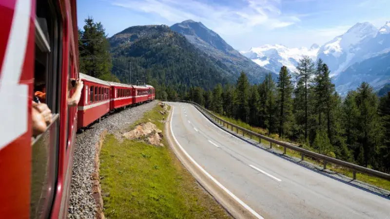 An image taken out of a red train carriage window as it takes a bend along a mountain pass, with the Swiss Alps in view.  
