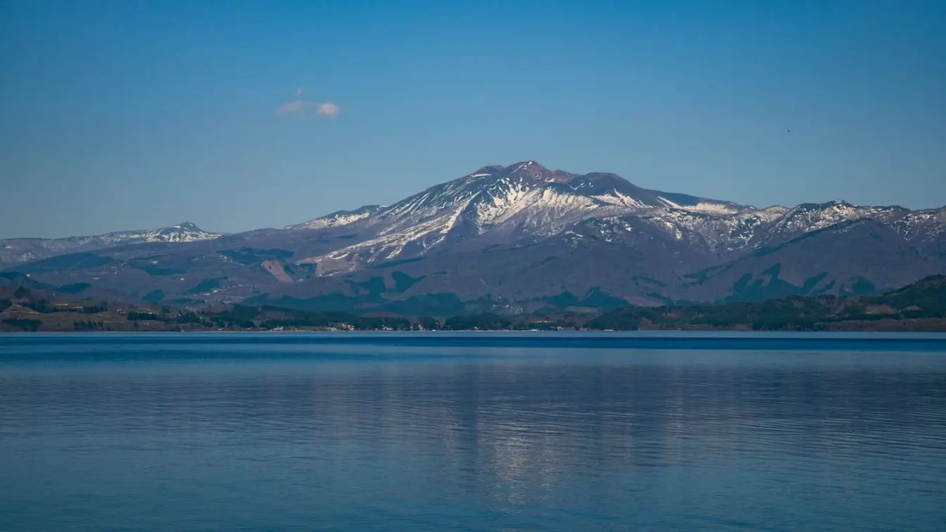 View of the blue water of Lake Tazawa with snow-dusted peaks in the background.