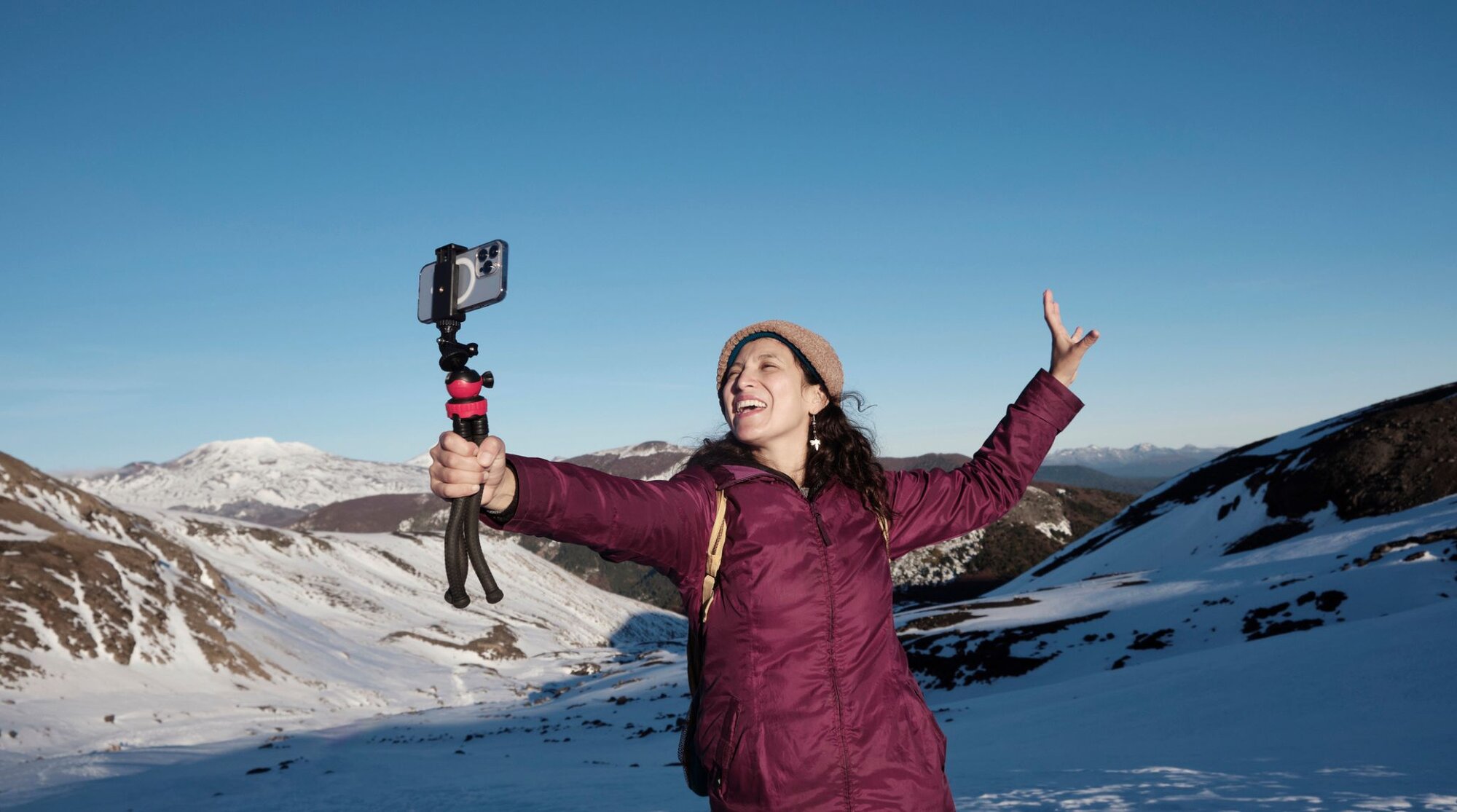 A woman is standing on a snowy mountain taking pictures with her phone using an Unlimited eSIM.
