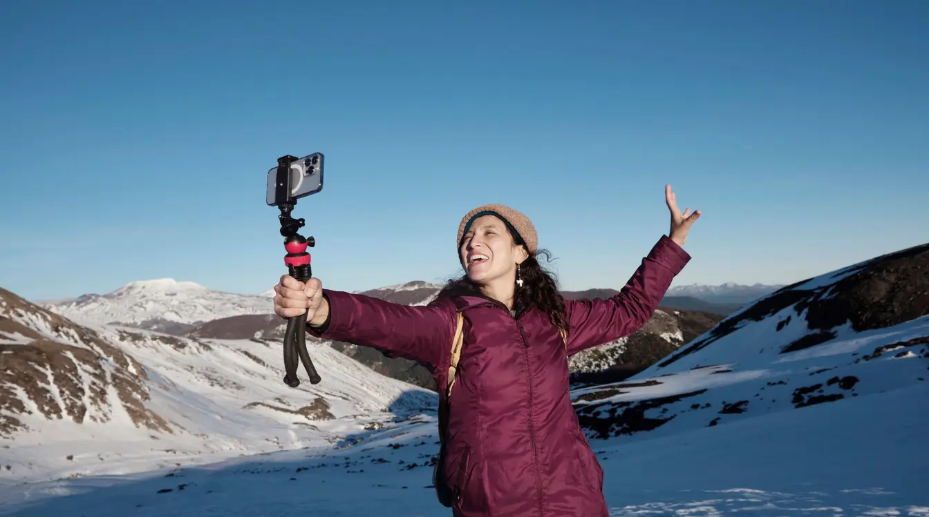 En kvinne står på et snødekt fjell og tar bilder med telefonen sin ved hjelp av et ubegrenset eSIM.