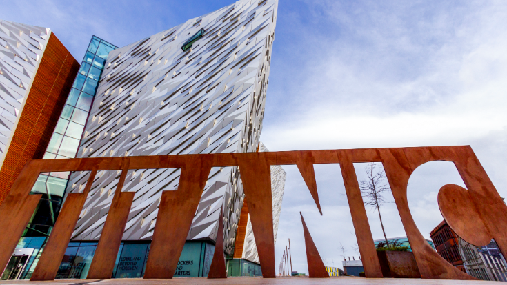 Belfast's Titanic museum, showing the main grey building and the giant sign bearing the cutout words 'TITANIC' in a rust finish.