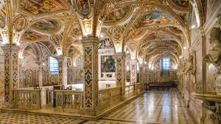 A colour photo inside the Crypt of San Matteo, featuring low-vaulted ceilings with Baroque frescoes and marble columns.