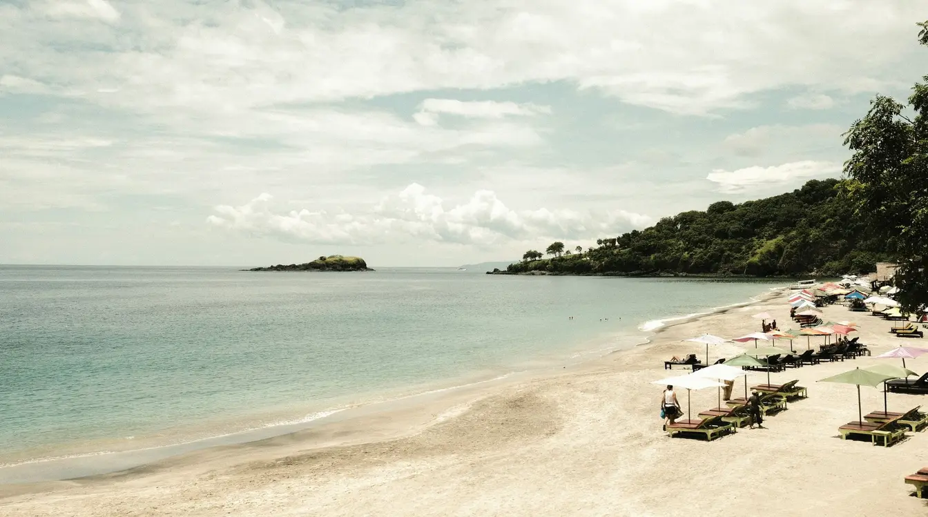 View of the sandy shore at Virgin Beach in Bali, partially lined with sunbeds and umbrellas.