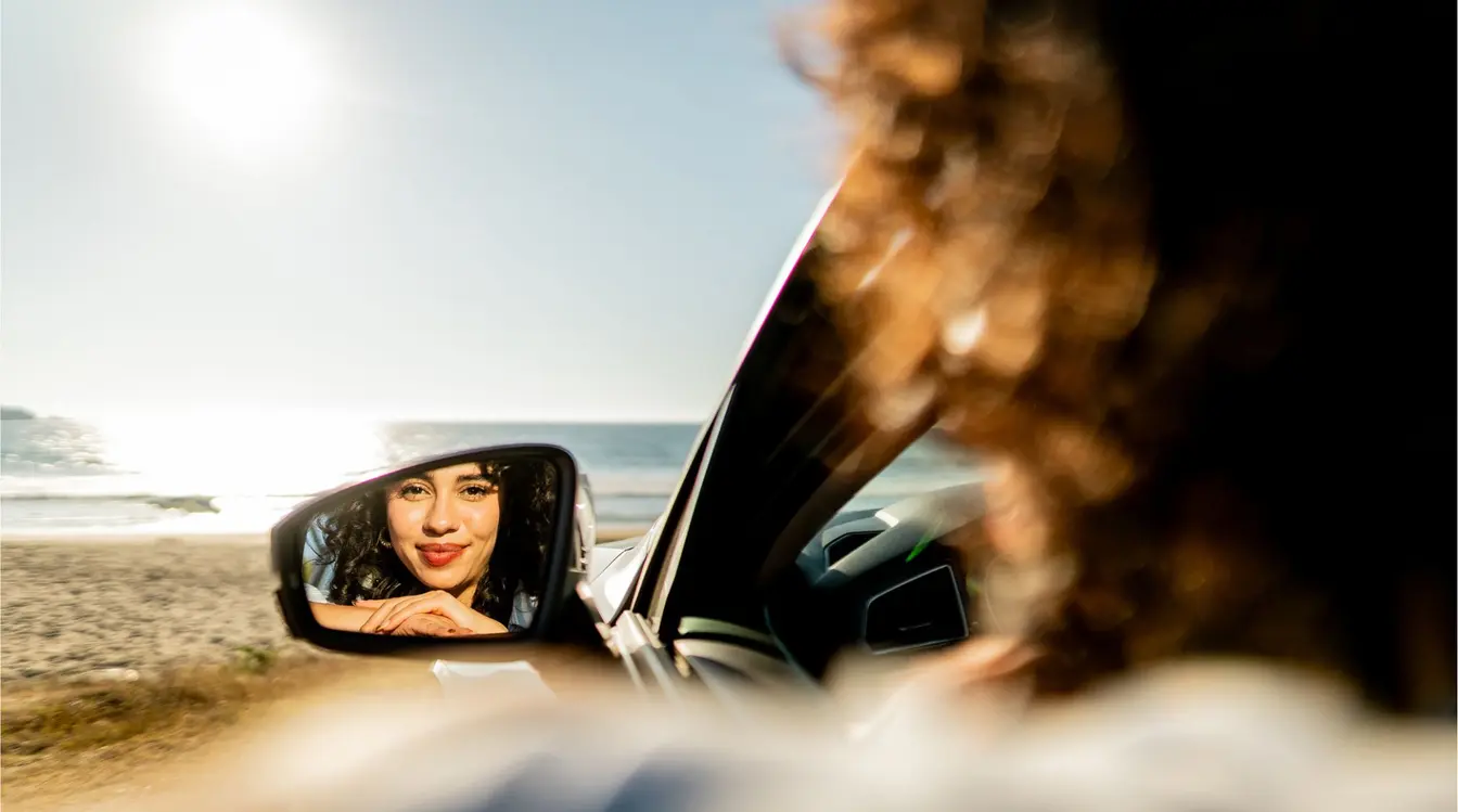 Mujer mirando el paisaje costero desde el espejo retrovisor durante un roadtrip en Baja California.