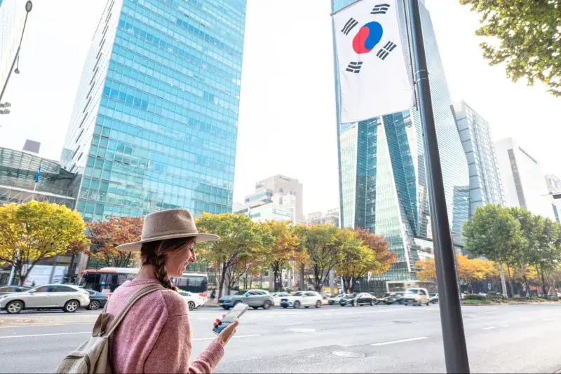ソウルの現代的な街並みを歩きながらスマートフォンを使う女性