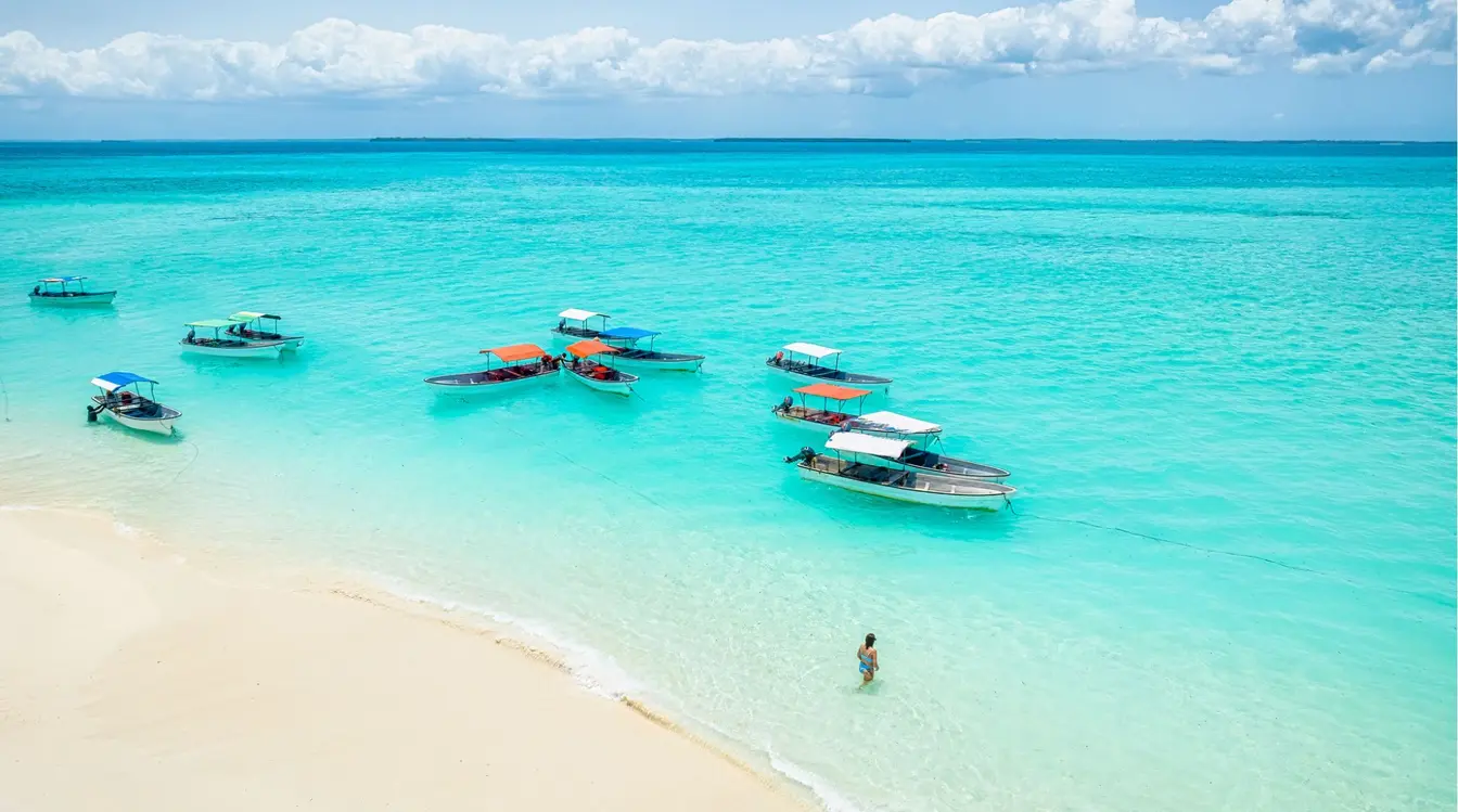 Vue aérienne de bateaux ancrés près d'une plage de sable blanc bordée par des eaux turquoise à Zanzibar.