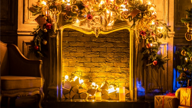 An image of a fireplace decorated with tinsel, baubles and other Christmas decorations in golds, greens and reds and shimmering over a lit log fire, to illustrate a blog post entitled 'Things to do in London in December'.