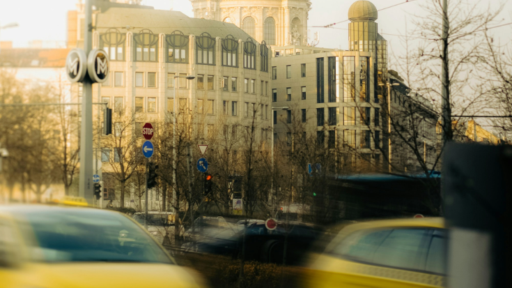 A photograph of Budapest city. In the foreground are blurred-out yellow taxis mid-journey. In the background are several grand looking buildings in a sandy beige colour. To illustrate a blog post entitled 'The Ultimate Sziget Festival Guide.'