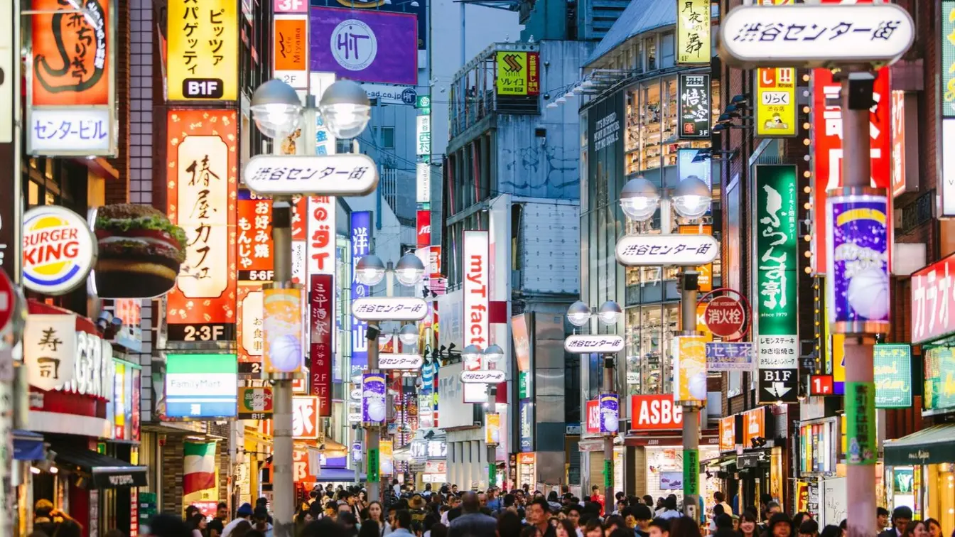 A crowded street with neon signs overhead in Tokyo’s Shibuya shopping district.