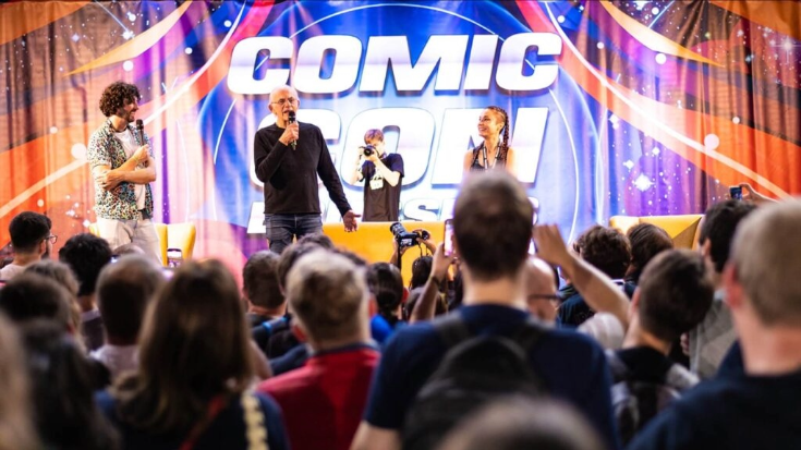 Actor Christopher Lloyd on stage with a microphone, with the Comic Con France logo behind him and crowds watching in front. 