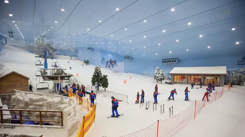 Inside Ski Dubai, showing a snow-covered ski run with people skiing down it, and a model wooden hut in the background.