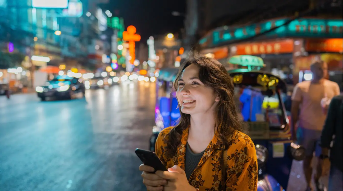 Voyageuse utilisant son smartphone près d’un tuk-tuk dans le quartier chinois de Bangkok.