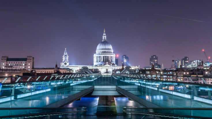 An image of St Paul's cathedral and its large dome in the night time against a dark sky, from across Millennium Bridge in London, to Illustrate a blog post entitled 'Things to do in London in December'.