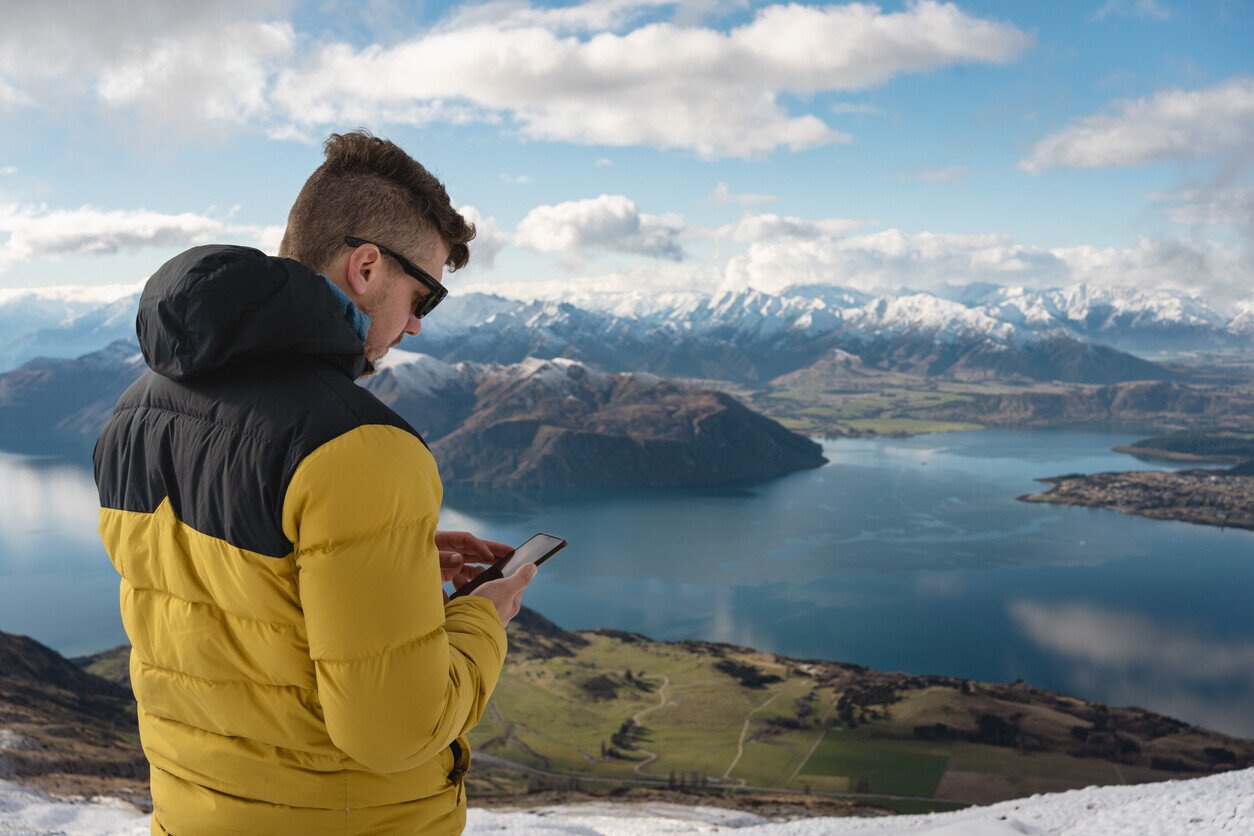 Mann auf einem Berg in Neuseeland mit Handy