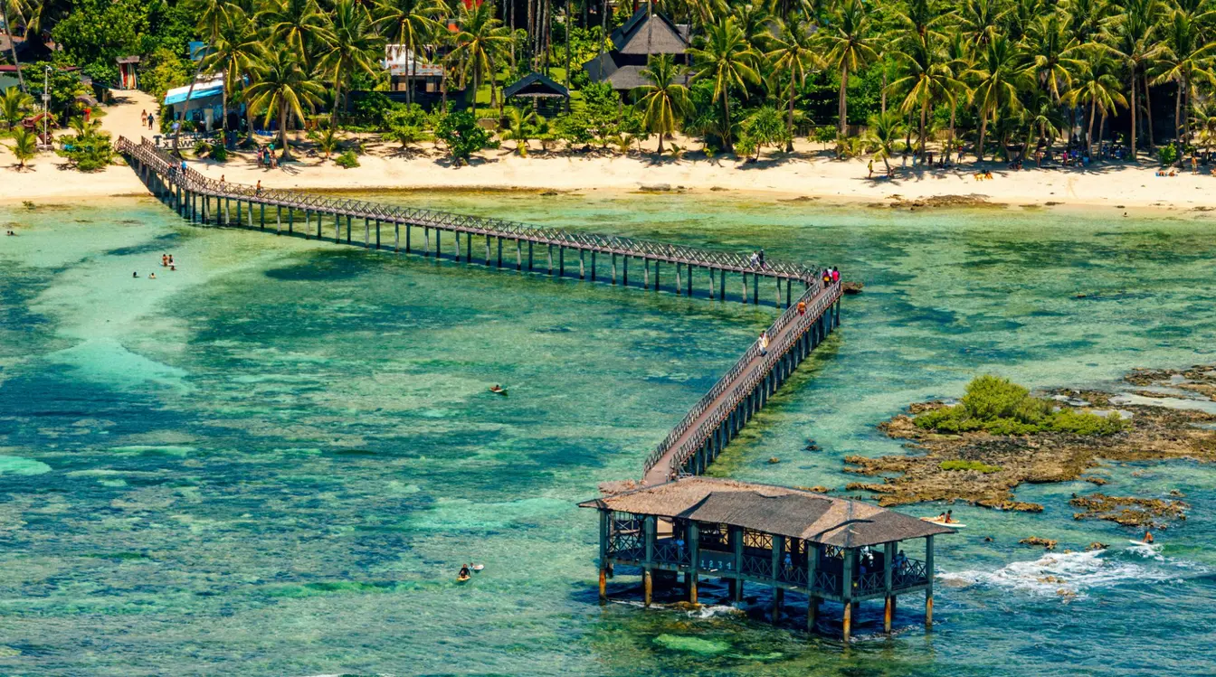 Aerial view of Cloud 9 and its iconic boardwalk on Siargao Island, with a handful of surfers in the sea.