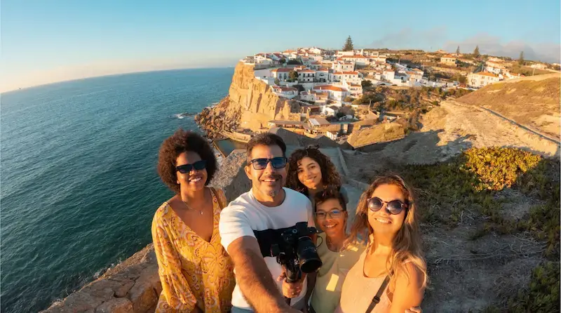 Grupo de turistas tomándose una selfie frente a un acantilado con vistas al océano durante un viaje en Portugal