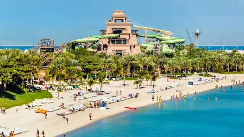 Aquaventure Waterpark in Dubai, showing a large snaking green slide winding around the main structure, surrounded by palm trees.