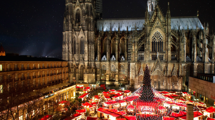 An image showing cologne's Gothic cathedral at night towering over the city's bustling Christmas markets.To illustrate a blog post entitled 'Extreme Day Trips: Eurostar Christmas Markets Edition'.