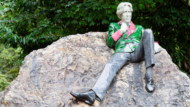 An image of a sculpture of the poet and playwright Oscar Wilde, which is placed in Dublin. It is made of copper and the figure is wearing a green and red jacket, to illustrate a blog post entitled Extreme Day Trips from London to Europe.