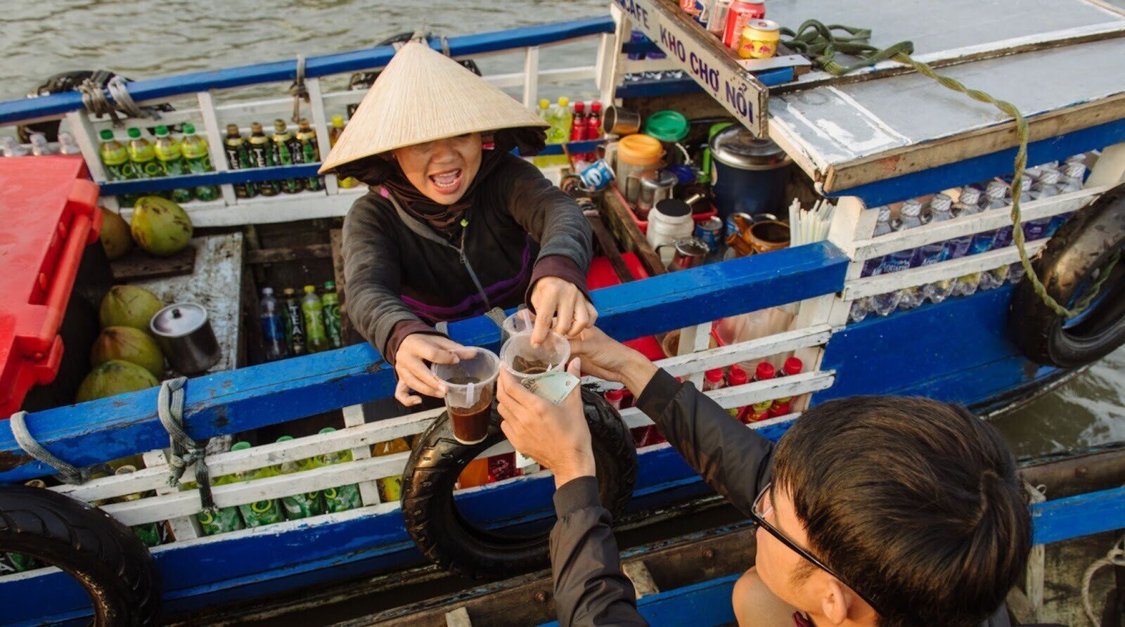 Voyageur payant en argent liquide vietnamien auprès d'une vendeuse de café sur un bateau du Mékong