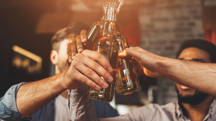 A close up of several men's hands as they hold bottles of beer in the air and clink them, as they watch the 2027 Six Nations in a bar in Paris. 